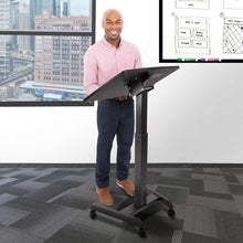 Black | Lifestyle image of a man with the black cruizer 360 featuring a tilting desktop and easy height adjustability presenting in a classroom setting.