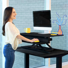black | 36-inch-desktop | Lifestyle image of the FlexPro Premier 36" electric standing desk converter in an office setting.